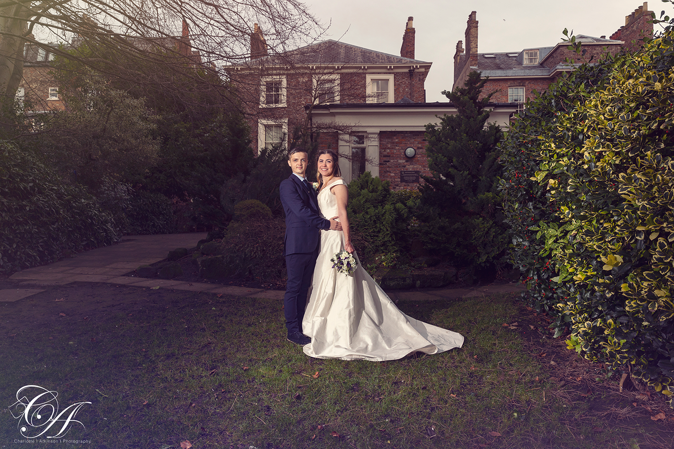 Bride and groom stood in the gardens of the York Register Office with the building in the background. York Wedding Photography