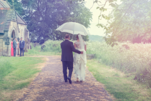 Bride and father walking to All Saints Church in the rain at Moor Monkton, York. Wedding Photography by Charlotte Atkinson