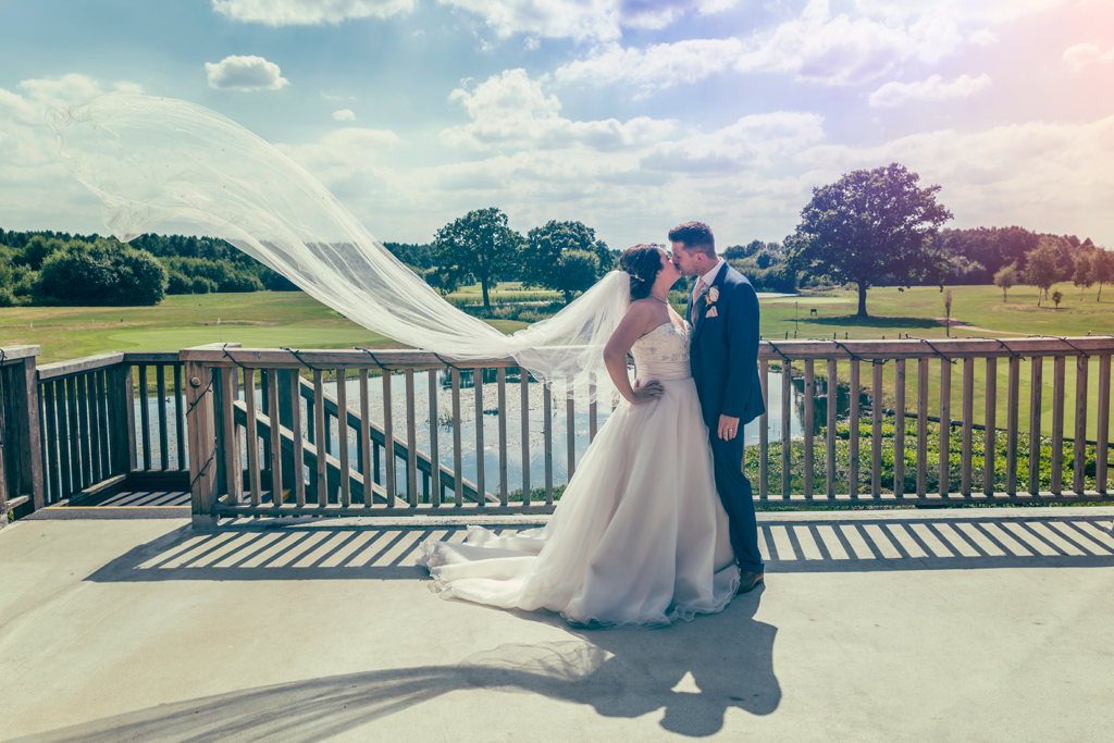 Bride and groom stood on the balcony at Sandburn Hall in York, with the vail blowing in the wind. Wedding Photography by Charlotte Atkinson