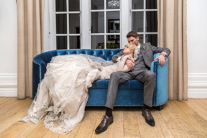 Groom sat on a blue sofa with the bride laid over him, at Woodlands Hotel in Leeds. Wedding Photography by Charlotte Atkinson Photography