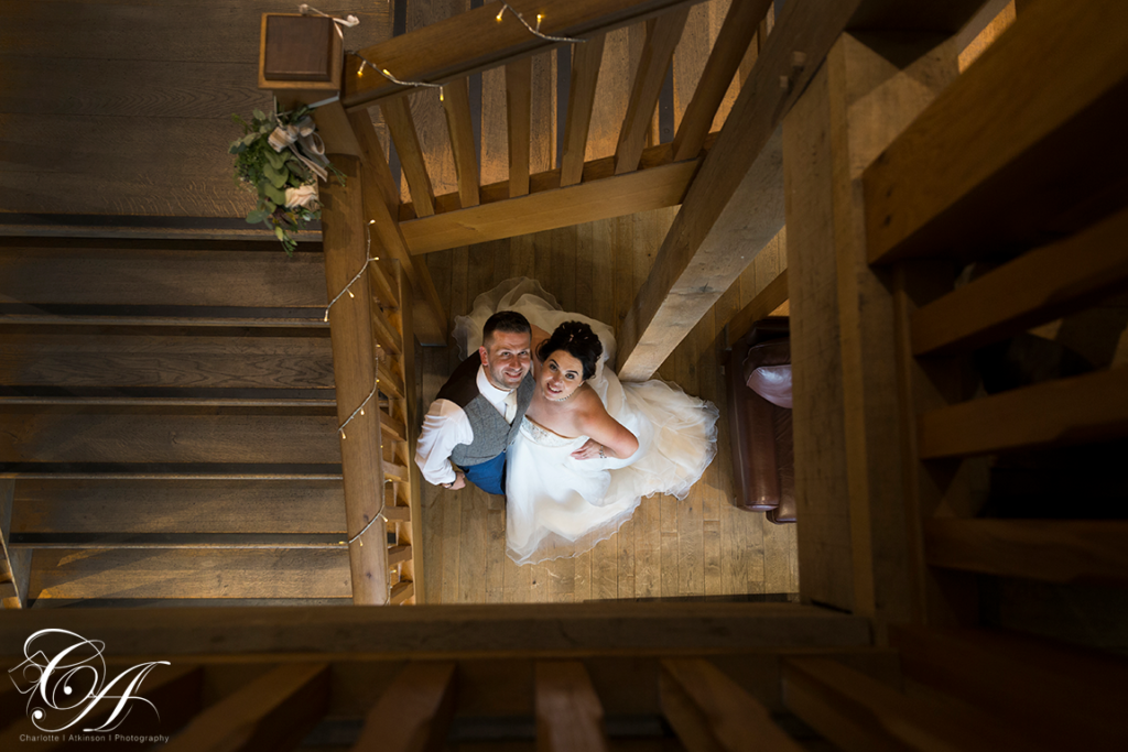 Bride and groom stood looking up to the York Wedding Photographer, who is taking the photo from the top of the stairs at Sandburn Hall, York.
