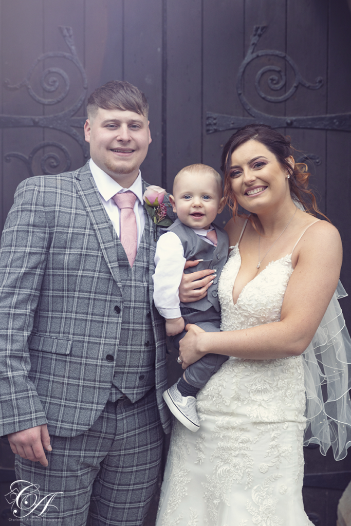 Bride and Groom and their baby stood in front of the church door. York Wedding
